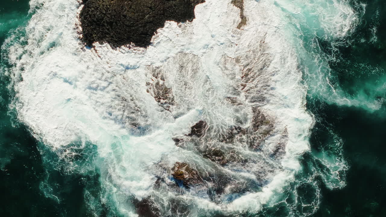 Spiral top down drone shot of rocky spur in the Atlantic Ocean with waves crashing during the day in Gran Canaria, Spain