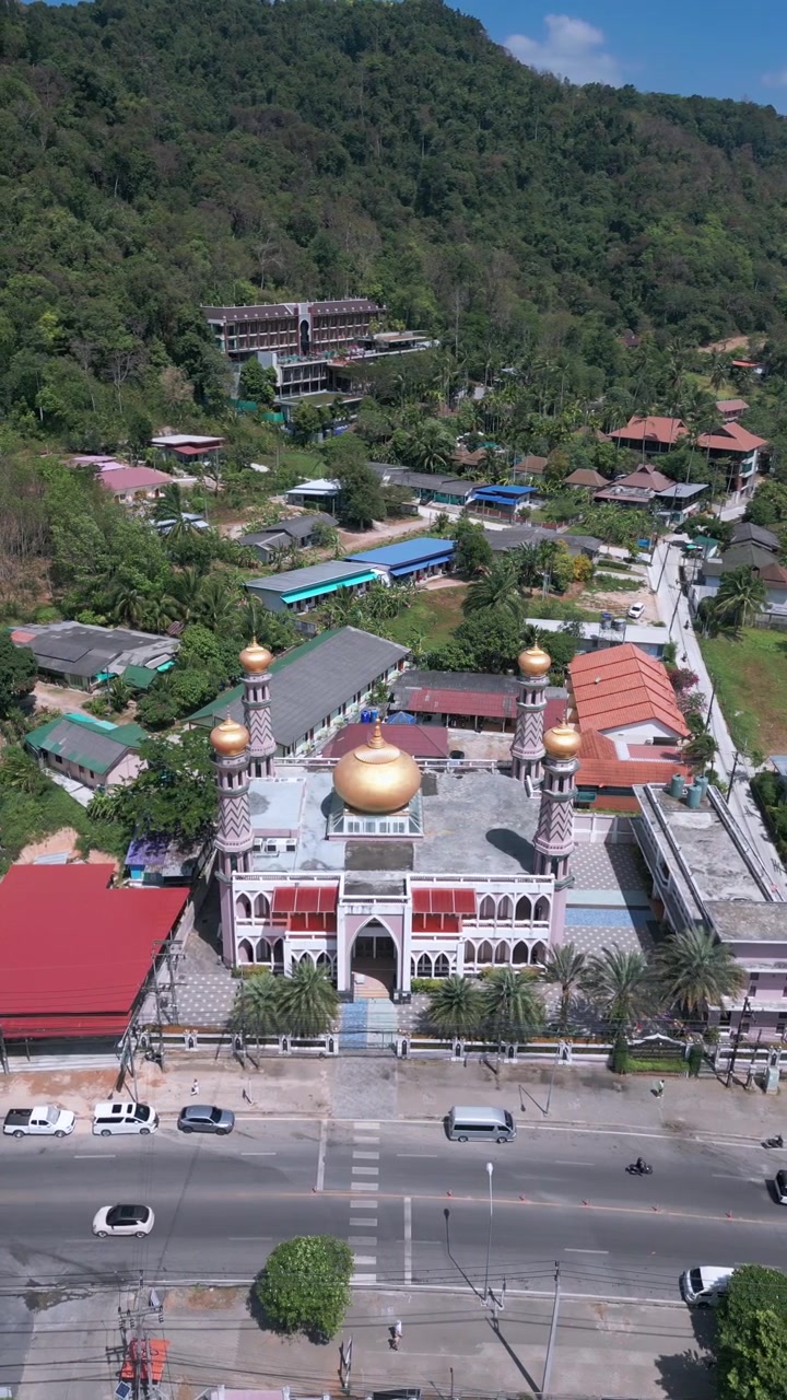 Penerbangan lateral di atas masjid berkubah emas dengan menara dan halaman yang dikelilingi oleh lereng bukit hutan tropis lebat. Ao Nang, Krabi, Thailand