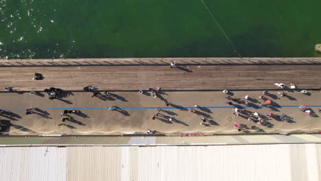 The-pedestrian-deck-in-the-old-Tel-Aviv-port-which-is-part-of-the-promenade-on-a-summer-day-with-many-visitors,-and-the-sea-water-beside-them---top-down-shot