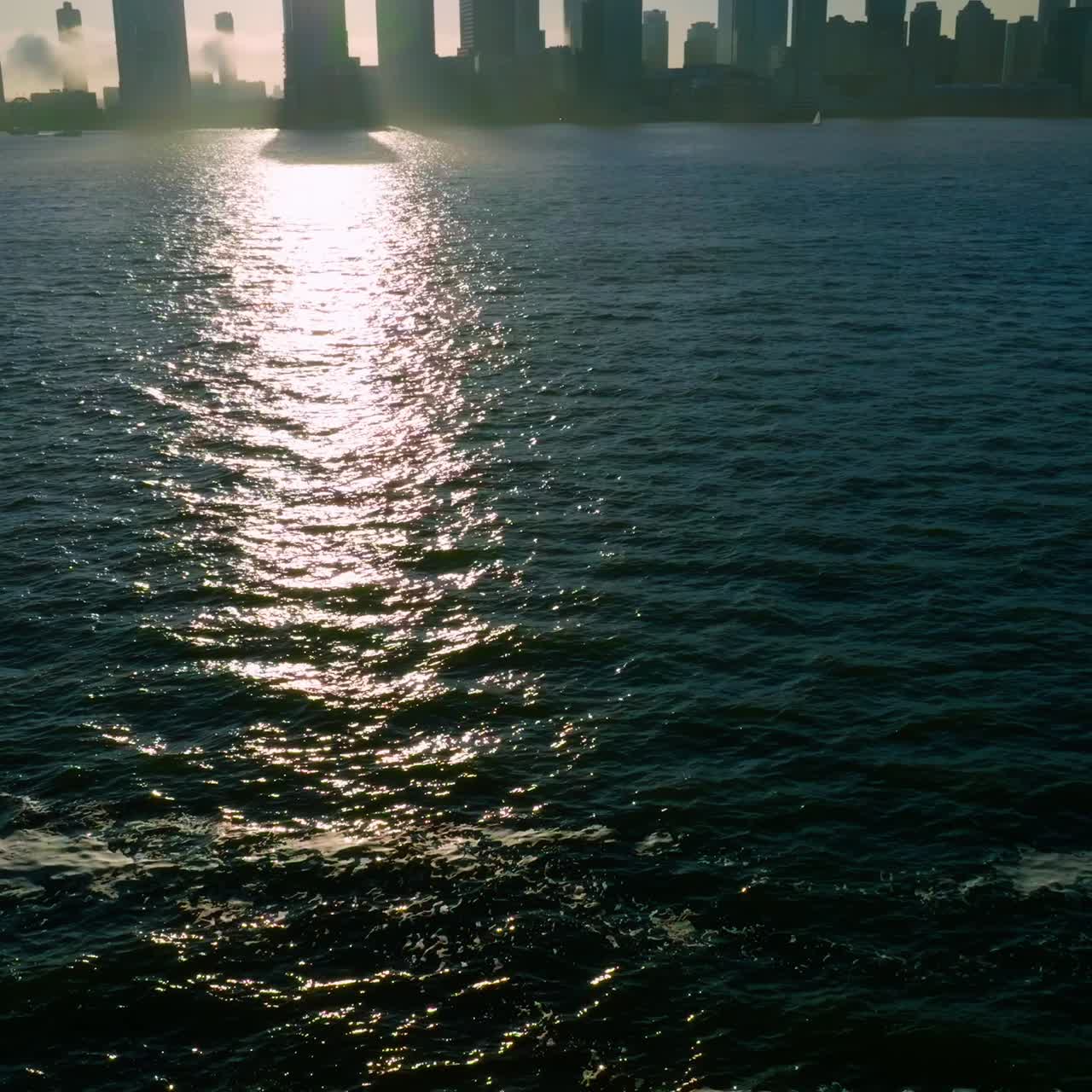 Dark silhouettes of skyscrapers at Manhattan Island. Sun reflecting in the dark water of Hudson river