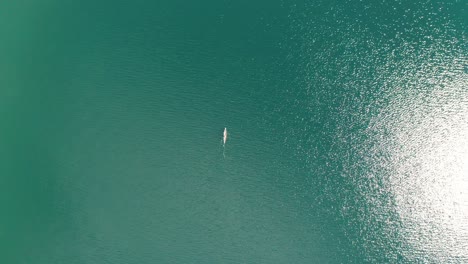 aérea de arriba hacia abajo, kayakista remando en un vasto lago turquesa