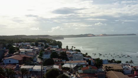 Rotating-aerial-drone-shot-of-the-famous-tropical-tourist-town-of-Pipa,-Brazil-in-Rio-Grande-do-Norte-with-a-group-of-boats-in-the-water-below-on-a-warm-sunny-summer-day