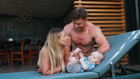 young parents resting with their infant baby. loving couple sit near the child lying on the deck chair.