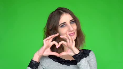 love. portrait smiling woman making heart sign, symbol with hands isolated green wall background.