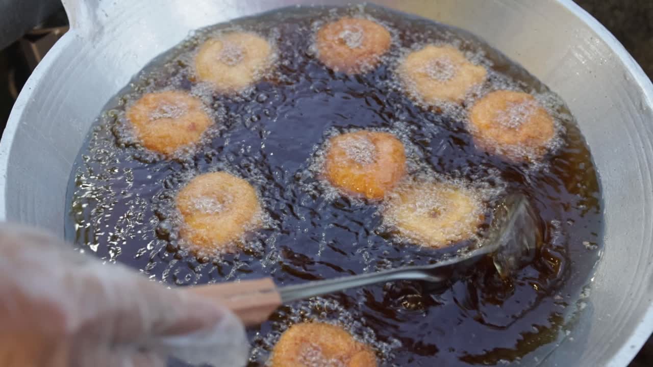 High angle of food vendor cooking rounded shape deep fried shrimp cake or Tod Mun Kung in Thai, in large amount of hot oil in a big wok at a local market