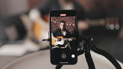 joven músico masculino transmitiendo un video tutorial, tocando la guitarra en casa