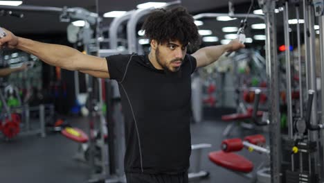 tipo rizado haciendo ejercicio en una estación múltiple en el gimnasio para los músculos de los brazos y los hombros, cámara lenta