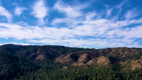 drone aerial push in time-lapse over mountain range covered with forest trees