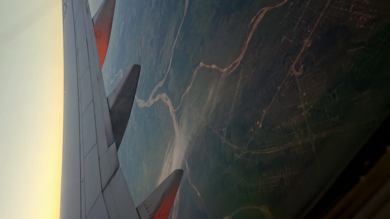 Tight Shot of an Airbus Airplane Wing in Flight at Dusk with Land Visible Below. Vertical