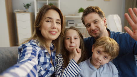 Pov-Of-The-Nice-Young-Family-Sitting-In-The-Cozy-Living-Room-And-Having-Videochat-With-Somebody