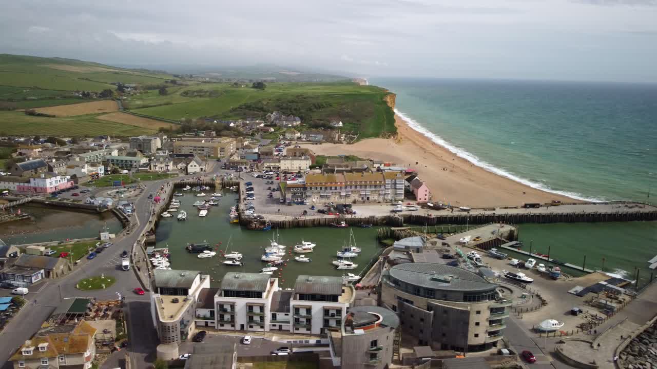 Drone video over the harbour of West Bay, Dorest. Orbit, sideways movement over the town, the buildings, boats with the beach and cliffs behind