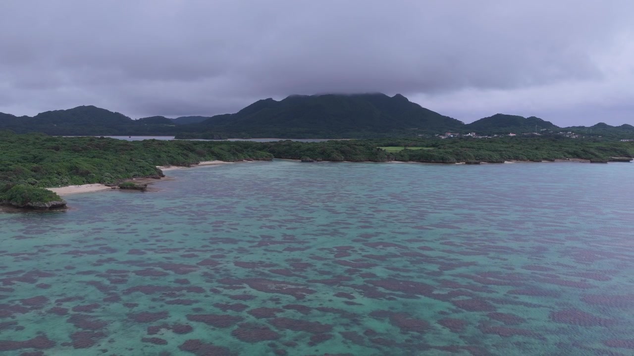 Riprese aeree orizzontali in dolly all'indietro sopra la barriera corallina e le acque turchesi di Yoshihara Beach vicino a Kabira, Isola di Ishigaki, Okinawa, Giappone