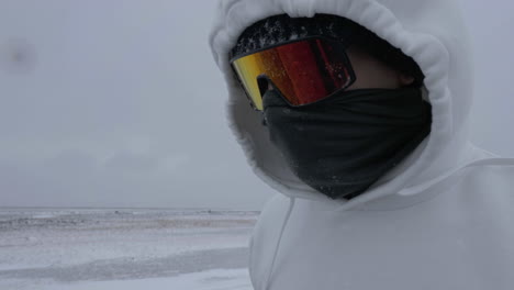 Unrecognizable-Man-in-Hoodie-With-Snow-Goggles-and-Mask-Walking-on-Snowfall-in-Cold-White-Winter-Landscape