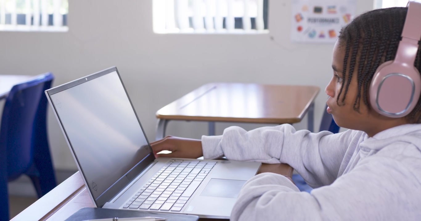 African American youth reaching for laptop trackpad with pink headset, studying at desk, copy space