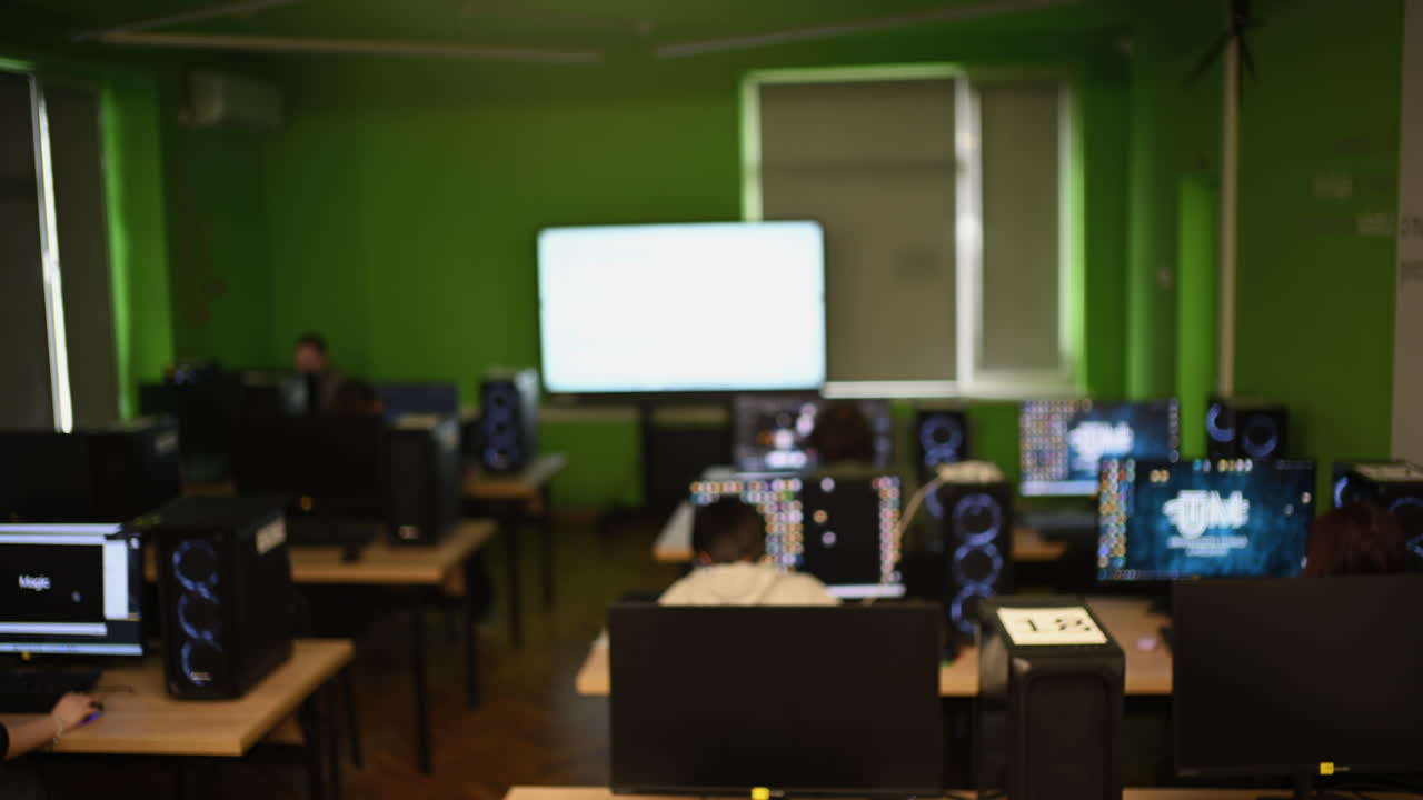 Vista amplia de un laboratorio de computación con múltiples estaciones de trabajo y estudiantes trabajando.