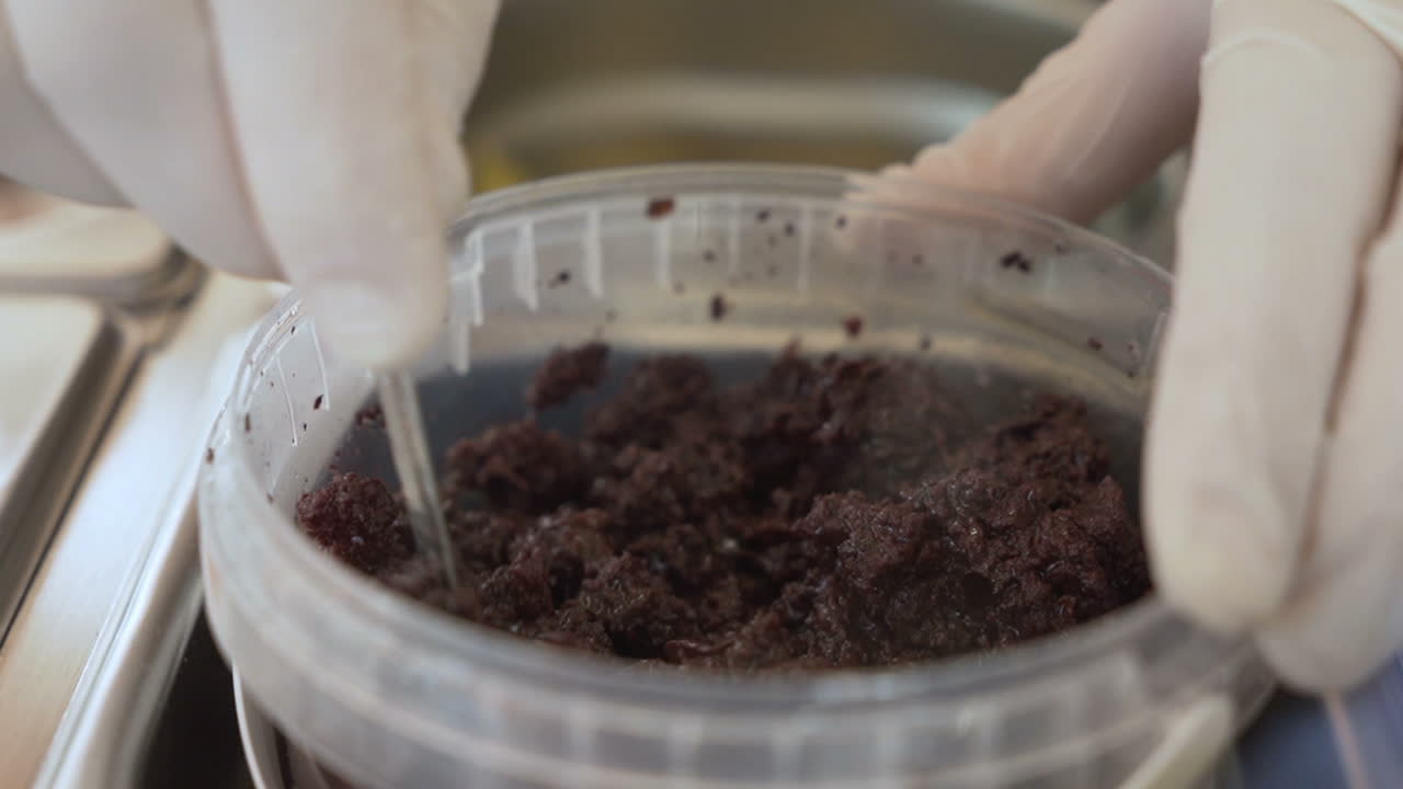 Mani maschili con i guanti mescolano tapenade di olive nere con un cucchiaio d'argento, primo piano.