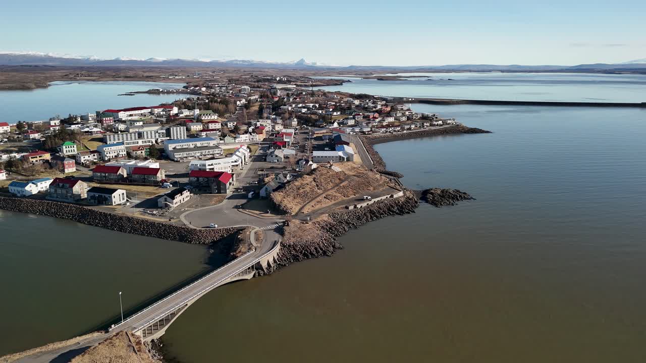 Drone video flying over the small town of Borgarnes surrounded by calm fjord water sitting at the foot of a beautiful mountain range in Iceland