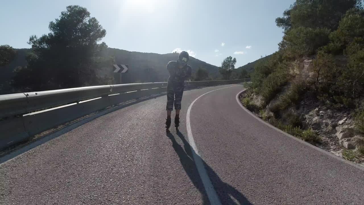 Front facing follow shot of roller skater going downhill on mountain road