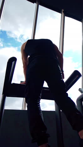 sportsman on treadmill in gym. guy in sportswear standing on a treadmill and doing running exercise on window background. back view from below. vertical video