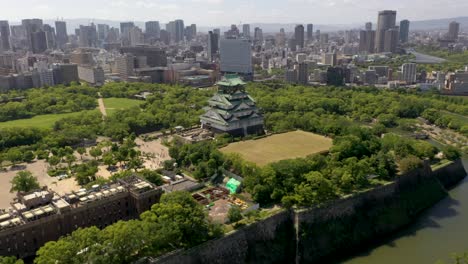 Aerial-of-famous-Osaka-Castle-with-park,-moat,-skyscraper,-and-city-in-Osaka,-Japan