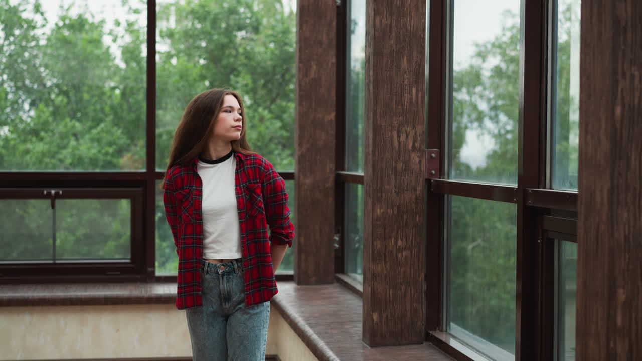 mujer molesta camina a lo largo de la terraza de vidrio de la cabaña. dama pensativa de mal humor trata de calmarse mirando el jardín detrás de la ventana. emociones negativas y salud