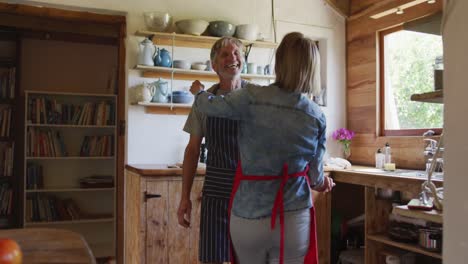 pareja caucásica mayor sonriente usando delantales y bailando antes de cocinar en la cocina