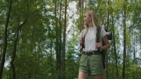 slow motion portrait: adult caucasian blonde woman wearing shorts and t-shirt hikes through woods. young lady hiking