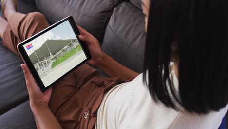 compuesto de una mujer sentada en casa en el sofá viendo un evento de salto de altura de atletismo en una tableta