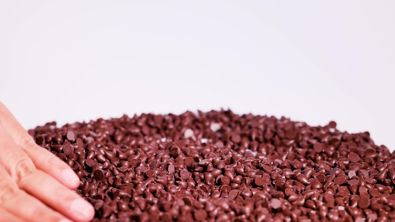 Hands gently sort chocolate drops on a white surface, creating a calming and tactile visual experience