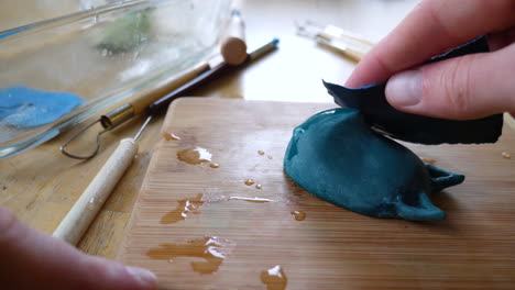 an artist sculpting, sanding, and polishing a polymer clay sculpture of a mask figurine with wet sand paper and art tools