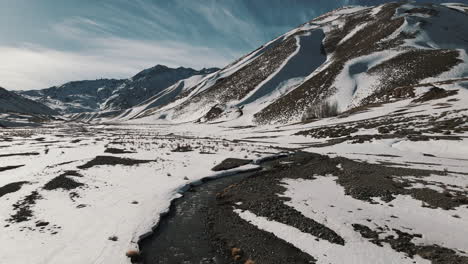 drone acelerando sobre un río en un valle andino nevado, capturando la impresionante belleza del paisaje montañoso