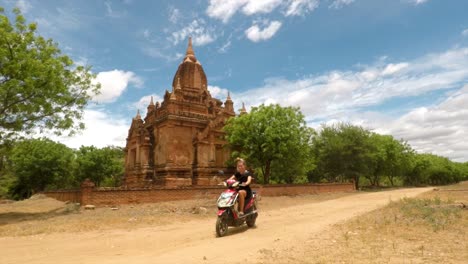 girl rides motorbike on quiet road in front of a large temple