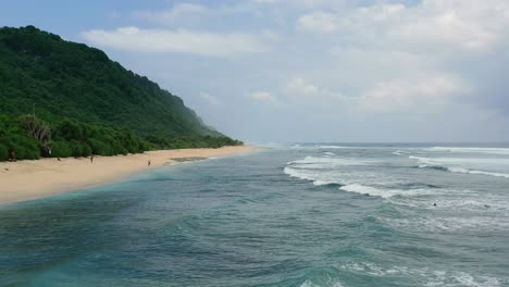 coastline beach with ocean waves crash on island with tall mountains, aerial