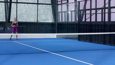 woman playing padel tennis on indoor court, holding racket and smiling