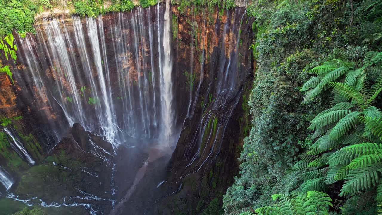 Rekaman udara drone yang menampilkan Air Terjun Tumpak Sewu di Jawa Timur, tempat lusinan aliran turun di atas tebing batu kapur berlumut ke ngarai sungai yang berkelok-kelok, dikelilingi oleh vegetasi tropis yang lebat