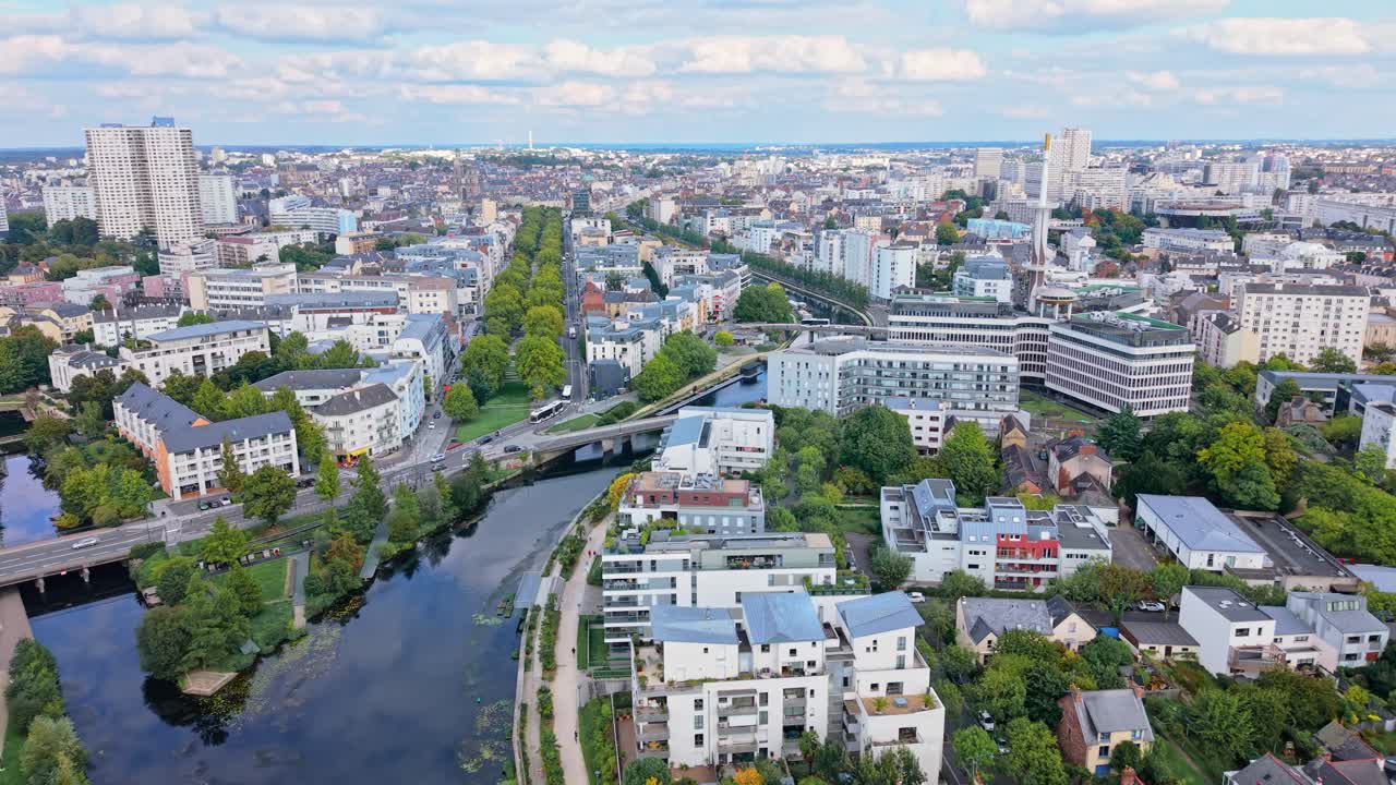 Drone flight over downtown Rennes, moving above the Vilaine River and the Mail François-Mitterrand, showing buildings, The Mabilais, Tower of Horizons, bridges, tree-lined avenues and the city