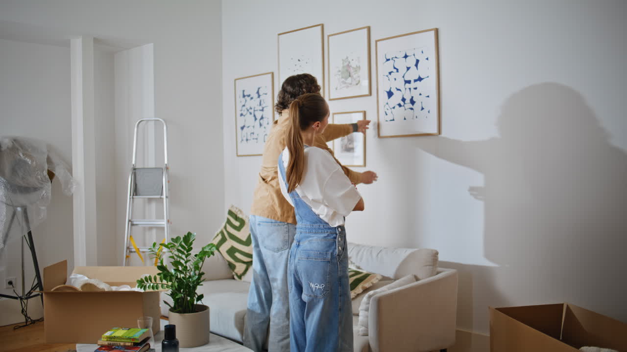 Married couple hanging artwork on wall new home. Spouses decorating living room