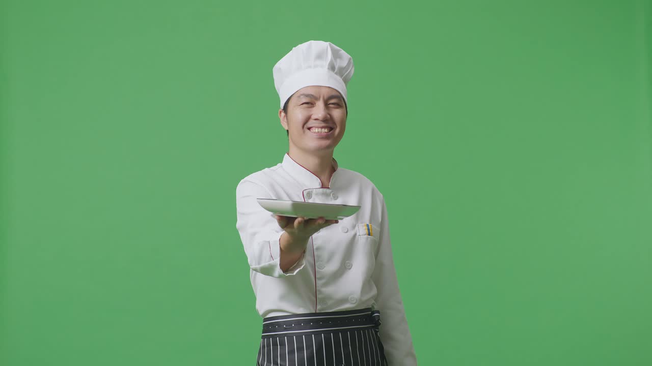 Asian Man Chef Smiling And Giving A Dish To Camera While Standing In The Green Screen Background Studio