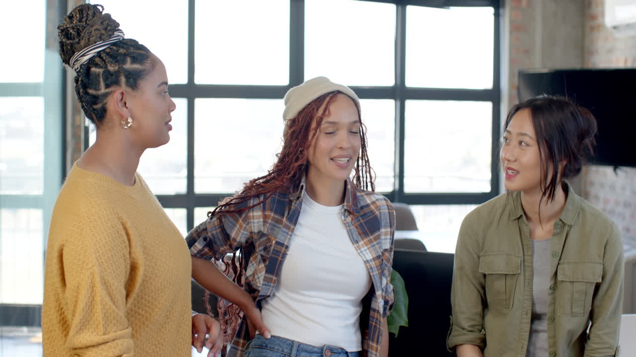 Laughing together, diverse female team in modern office collaborating on teamwork project