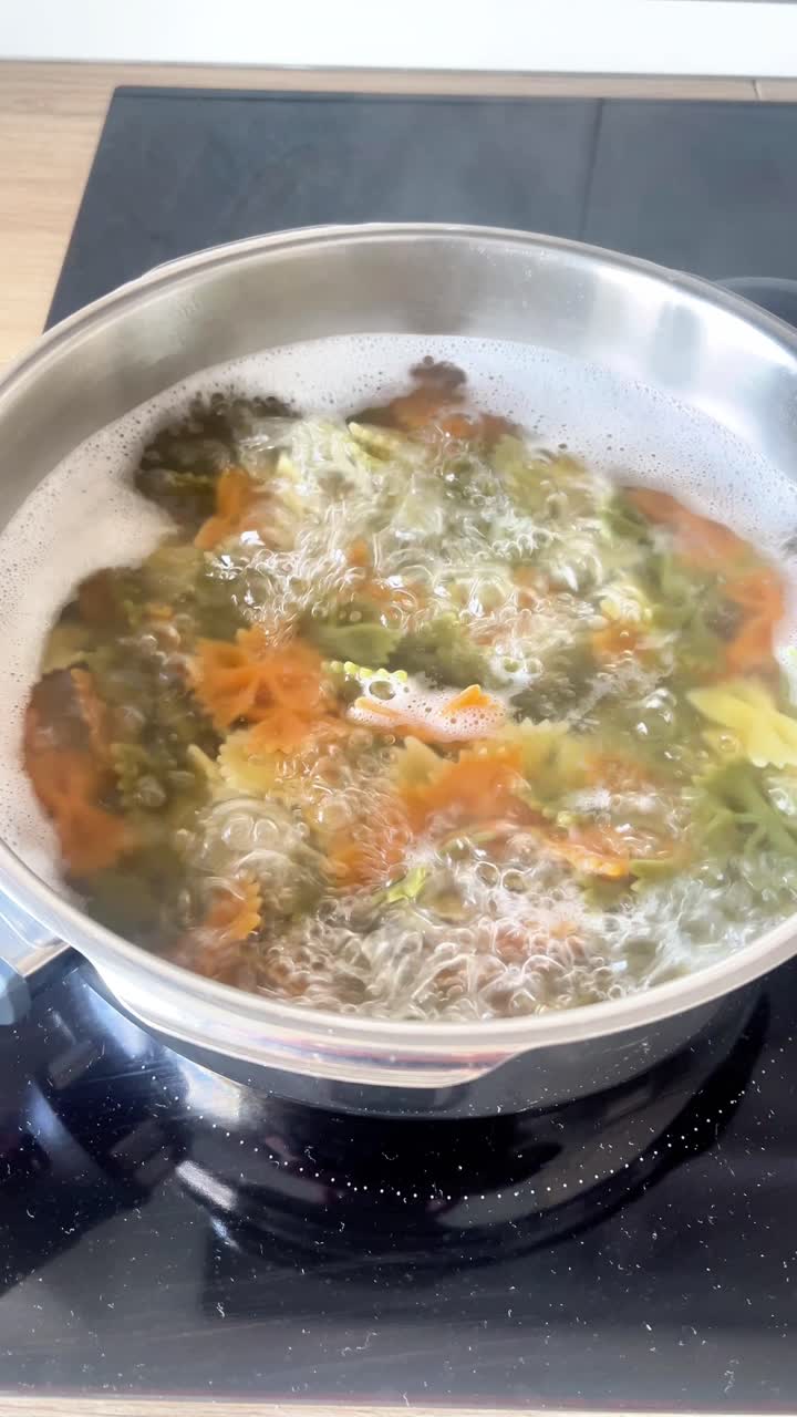 En gryde pasta koger på et komfur. Maden er en blanding af grøntsager og pasta