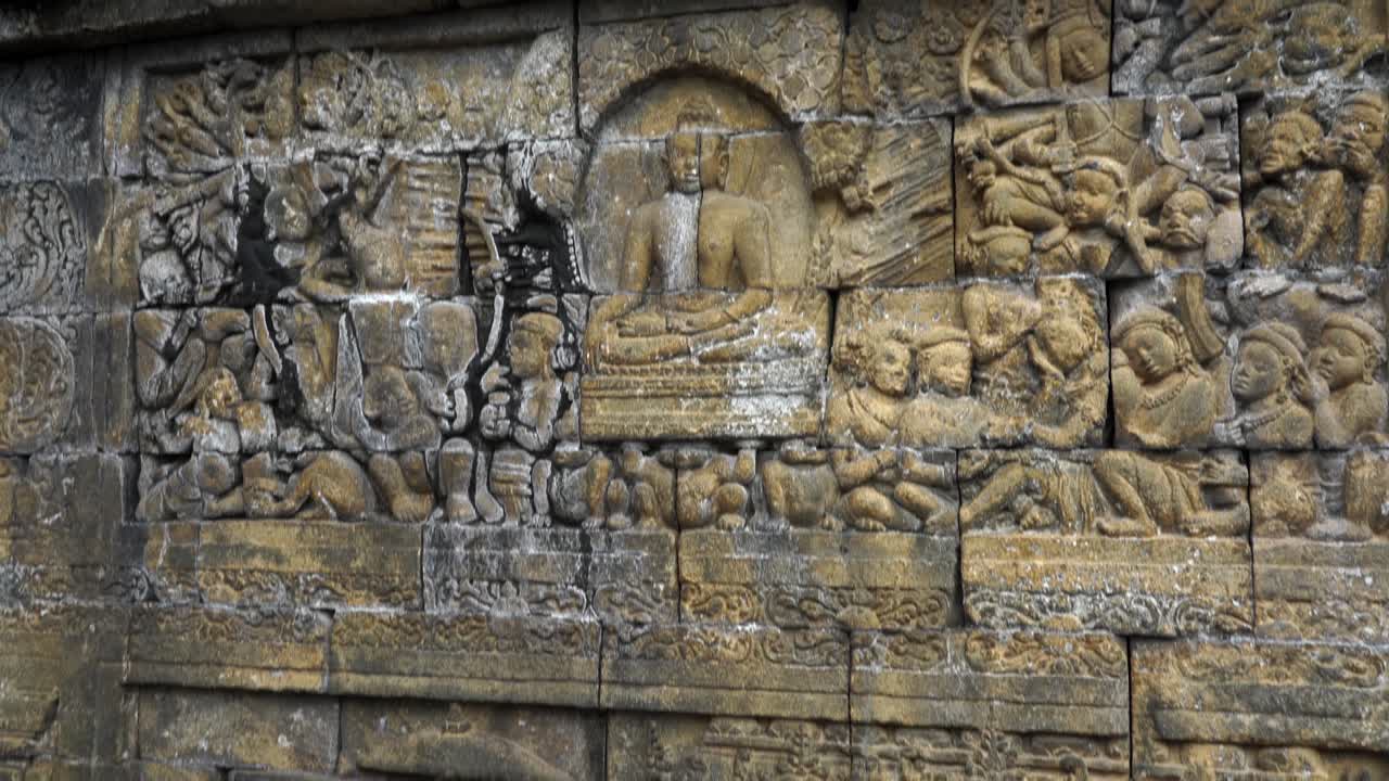 Indonesia, Isola di Giava, Yogyakarta. Interno del Tempio di Borobudur, patrimonio mondiale dell'UNESCO: primo piano di un rilievo murale. La telecamera si inclina lentamente verso l'alto, mostrando il rilievo nei dettagli e le antiche storie sulla parete.