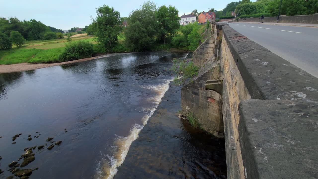 Wide shot of River Ure spilling over low weir next to road bridge in Ripon