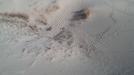 Trineo-De-Arena-En-Una-Duna,-Vista-Aérea-Del-Hombre-A-Bordo-Bajando-En-Una-Colina-Arenosa-En-El-Parque-Estatal-Monahans-Sandhills,-Texas-Usa,-Tiro-Con-Drones