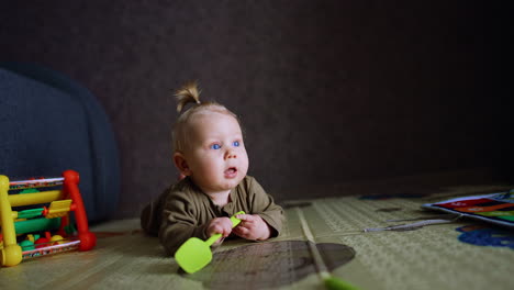 beautiful baby lies on belly on the floor. infant holding a toy shovel in hands. little balls are thrown to the kid.