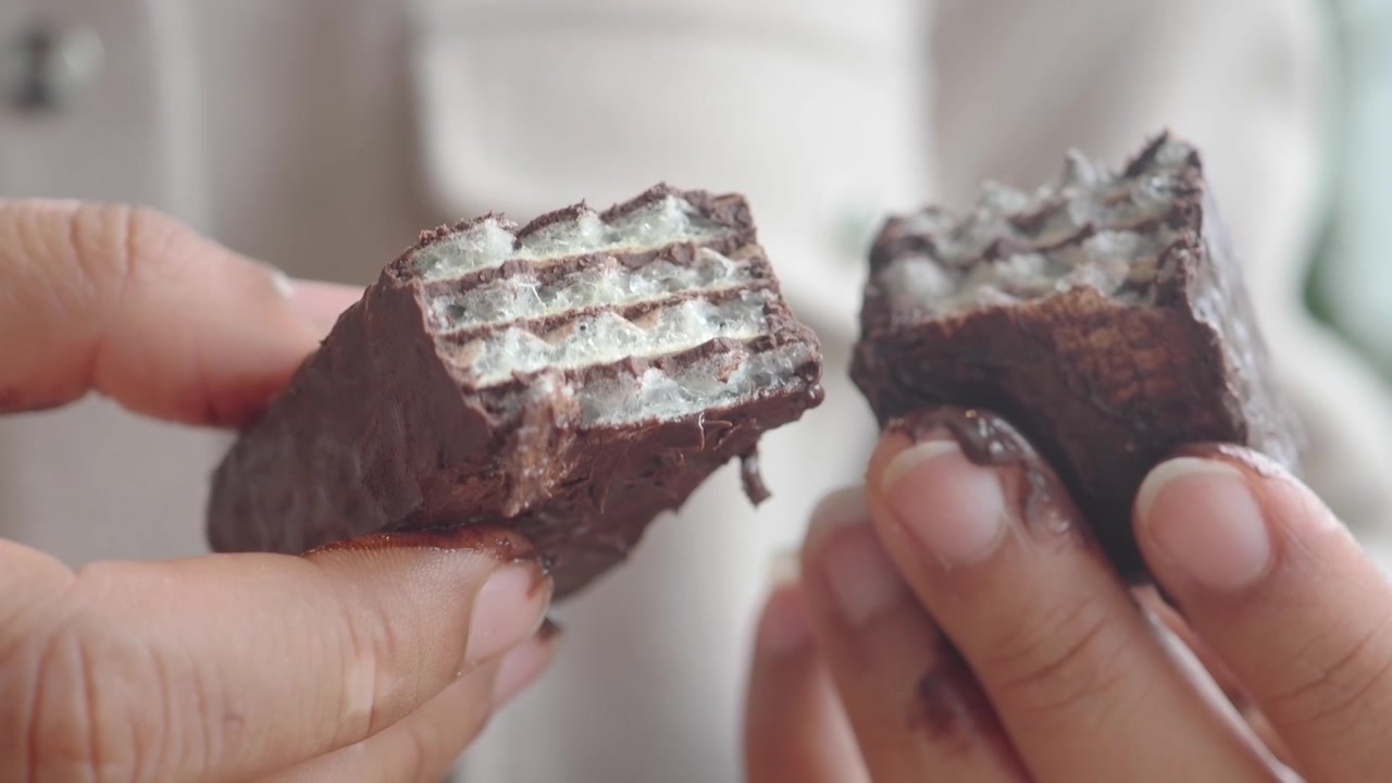Primo piano di mani che tengono una barretta di wafer al cioccolato rotta