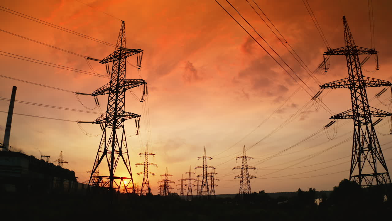 Tall electric towers at sunset. High voltage electric line distribute electricity through cables. Distribution station with metal pylons in the evening. Slow motion.