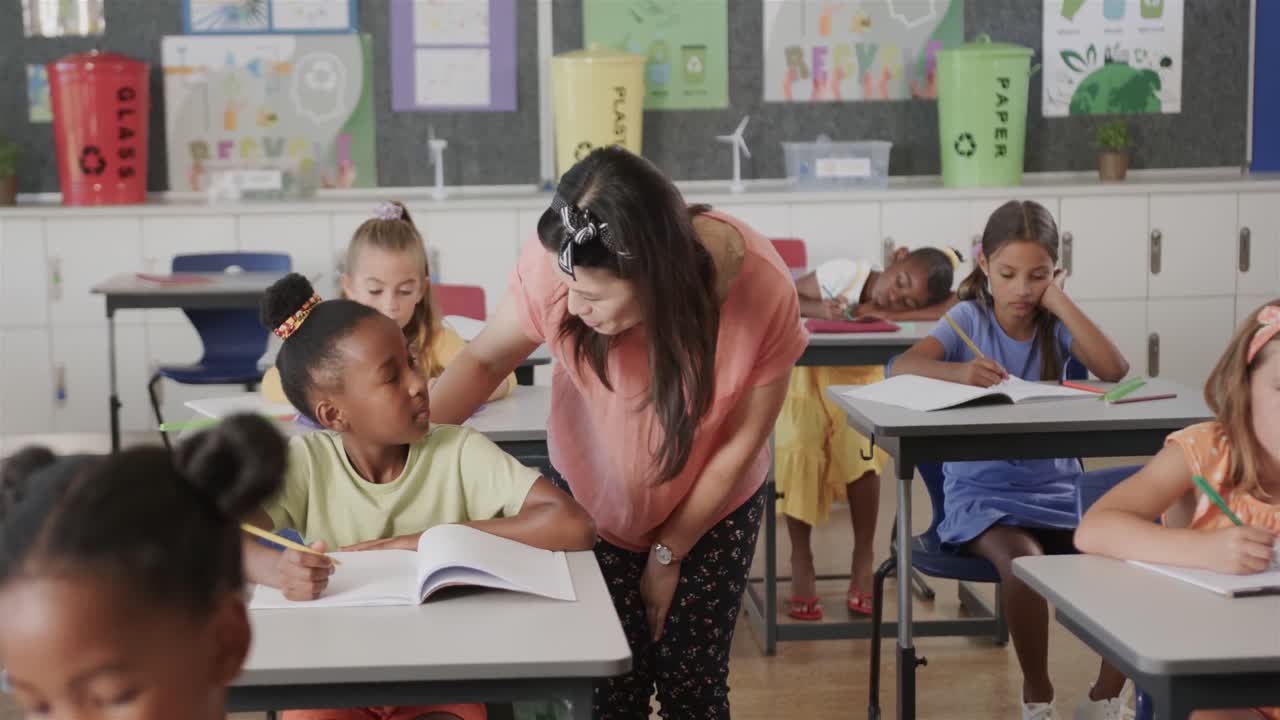 feliz maestra diversa ayudando a una colegiala en el escritorio en la clase de escuela primaria, cámara lenta