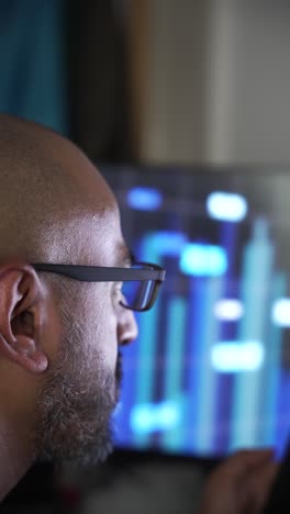 a focused south asian professional observing financial trends on a glowing chart displayed monitor. vertical video