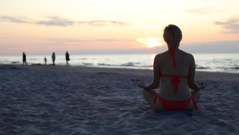 Schlanke-Frau-Im-Bikini-Während-Der-Ferien-Im-Badeort,-Die-Im-Lotussitz-Am-Meer-Meditiert