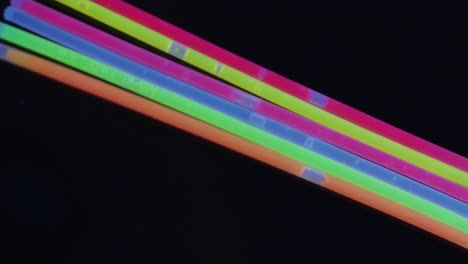 animation of colorful neon glow sticks over black background with copy space